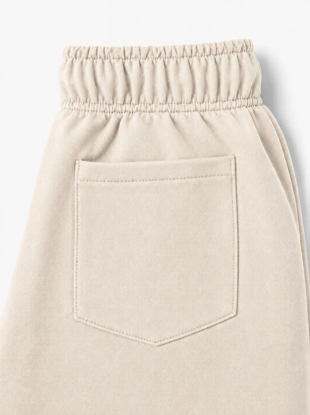 Close-up of a light beige or cream-colored garment, showing an elastic waistband and a single front patch